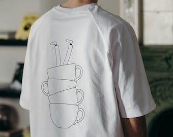May include: White t-shirt with a graphic of stacked cups and legs sticking out of the top.