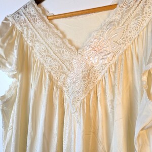 May include: A white satin nightgown with a lace trim and a floral design. The gown has short sleeves and a V-neckline.