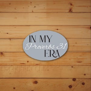 May include: A gray oval sign with the text "IN MY Proverbs 31 ERA" in black and white lettering. The sign is set against a light brown wooden background.