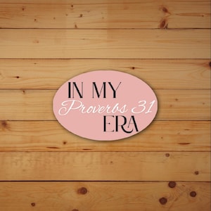 May include: A pink oval sign with the text "IN MY Proverbs 31 ERA" in black and white lettering. The sign is set against a light brown wooden background.