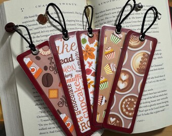 Könnte beinhalten: Fünf verschiedene Lesezeichen mit verschiedenen Designs. Die Lesezeichen sind alle rechteckig und haben einen roten Rand. Die Designs beinhalten Kaffee, Cupcakes und Herbstblätter. Die Lesezeichen sind alle aus Papier und haben eine glänzende Oberfläche.