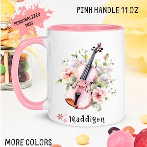May include: White ceramic mug with a pink handle and interior. The mug features a watercolor illustration of a pink violin surrounded by flowers. The name "Maddison" is printed on the mug. The mug holds 11 oz.