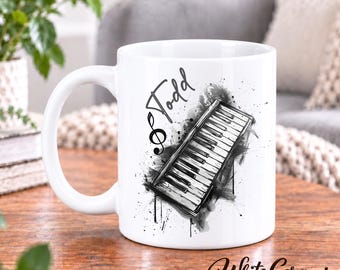 May include: A white ceramic mug featuring a black and white ink-style illustration of a piano keyboard and a treble clef. The name Todd is printed in a script font above the keyboard graphic. The mug has a standard handle and a smooth finish.