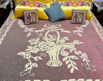 May include: A bed with a burgundy crocheted bedspread featuring a floral basket design. The bed has yellow velvet pillows with floral embroidery, a blue patterned pillow, and two small square pillows with intricate patterns.