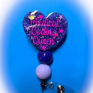 May include: A retractable badge reel with a heart-shaped design. The heart is purple with glitter and the words "Medical Coding Queen" in pink. It has a crown and star accents. The reel has purple and lavender beads.