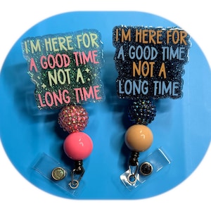 Puede incluir: Dos carretes de insignia con el texto "I'M HERE FOR A GOOD TIME NOT A LONG TIME". Uno tiene un diseño rosa y brillante, el otro un diseño negro y brillante. Ambos tienen un acento de cuentas y una bola rosa o beige.