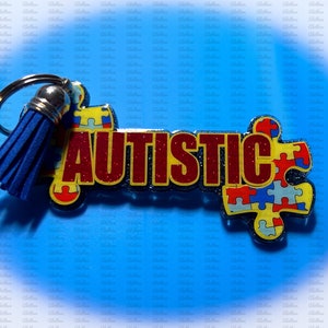 May include: A blue tassel keychain with the word "AUTISTIC" in red glitter letters and a puzzle piece design in blue, yellow, and red.