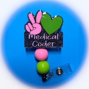 May include: A black glitter badge holder with a pink peace sign and green heart, with the text "Medical Coder". The badge holder has a pink and green beaded retractable badge reel.
