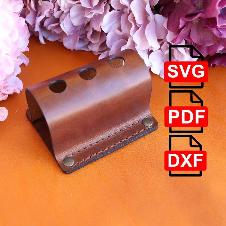 May include: A brown leather toothbrush holder with three slots and a stitched edge. The holder has two brass rivets. The image also includes text that says "SVG", "PDF", and "DXF".