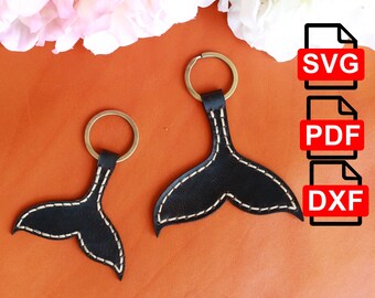 May include: Two leather keychains shaped like a whale tail. The keychains are brown with white stitching and have a gold metal ring. The keychains are on a brown surface. SVG, PDF, and DXF file types are listed on the right side of the image.