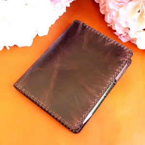 May include: A brown leather notebook with a stitched edge and a green interior. The notebook is on a bright orange surface.