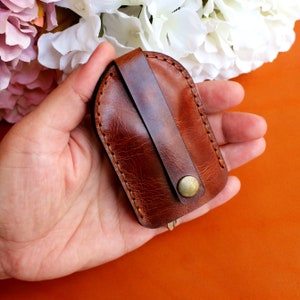 May include: A brown leather key holder with a stitched edge and a brass button closure.