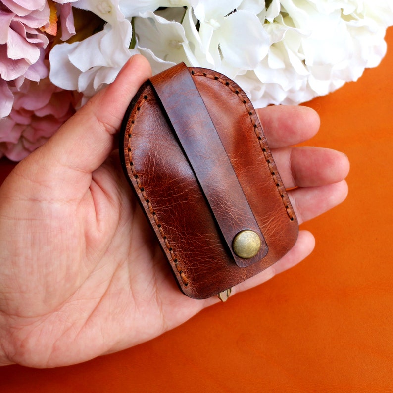 May include: A brown leather key holder with a stitched edge and a brass button closure.