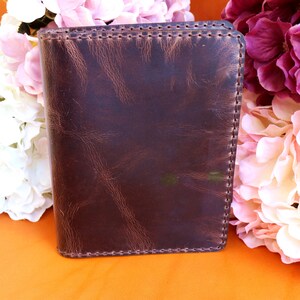 May include: A brown leather notebook with a stitched edge. The notebook is closed and has a distressed look.