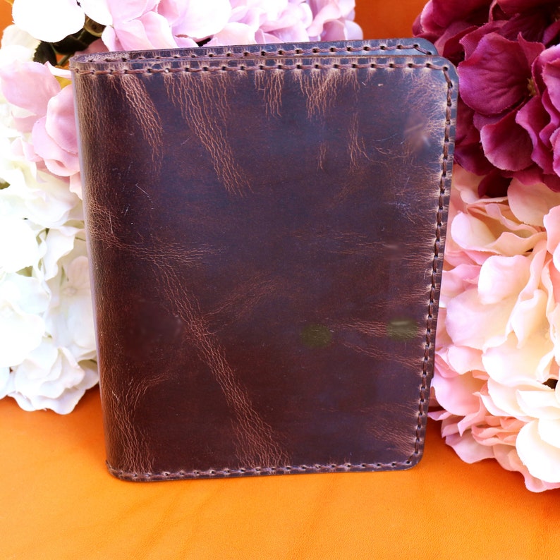 May include: A brown leather notebook with a stitched edge. The notebook is closed and has a distressed look.