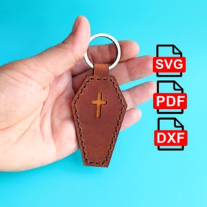 May include: A brown leather keychain shaped like a coffin with a silver cross cutout. The keychain is attached to a silver key ring. The image also shows three file format icons: SVG, PDF, and DXF.