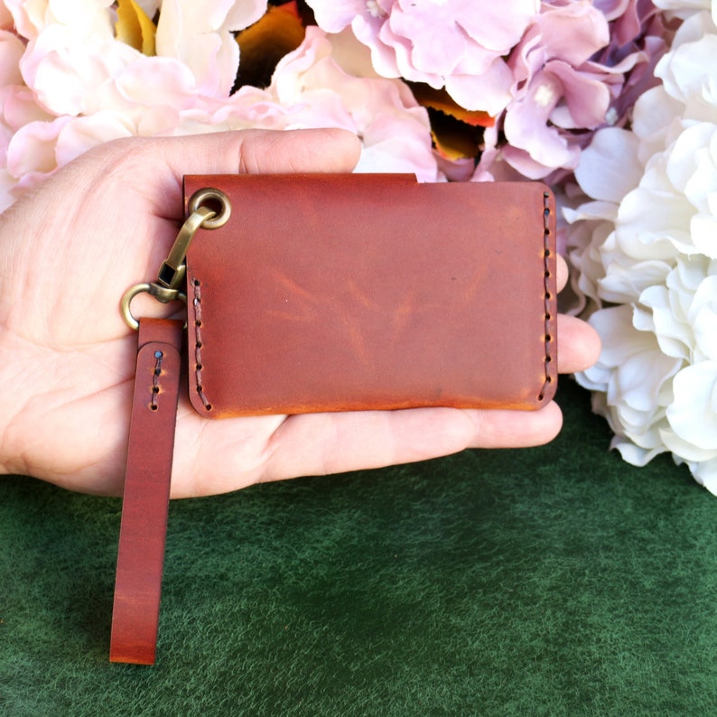 May include: A brown leather wallet with a stitched edge and a brass chain attached to a brown leather strap.
