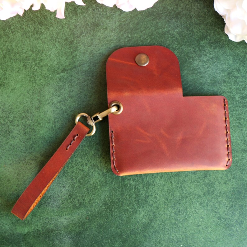 May include: A brown leather wallet with a strap and a brass clasp. The wallet is closed and has a worn, distressed look.