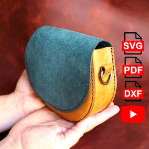 Può includere: Borsa a tracolla in pelle fatta a mano con patta in camoscio verde acqua e corpo in pelle marrone chiaro. La borsa presenta un design cucito, un anello di metallo e una forma curva. L'immagine include anche icone per file SVG, PDF e DXF e un pulsante di riproduzione di YouTube.