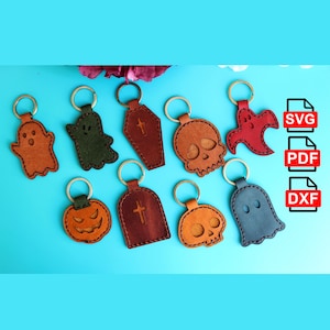 Puede incluir: Nueve llaveros de cuero con temas de Halloween, que incluyen un fantasma, una calabaza, una calavera y un ataúd. Los llaveros están sobre un fondo azul. También se incluyen archivos SVG, PDF y DXF.