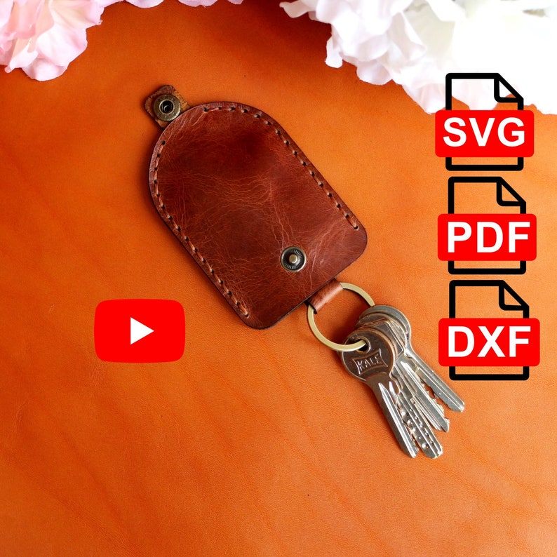 May include: Brown leather key holder with a metal ring and keys attached. The key holder has a stitched edge and a metal button. The image also includes a red play button and text that says "SVG", "PDF", and "DXF".