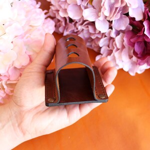 May include: A brown leather holder with three holes for storing items. The holder is held in a hand.