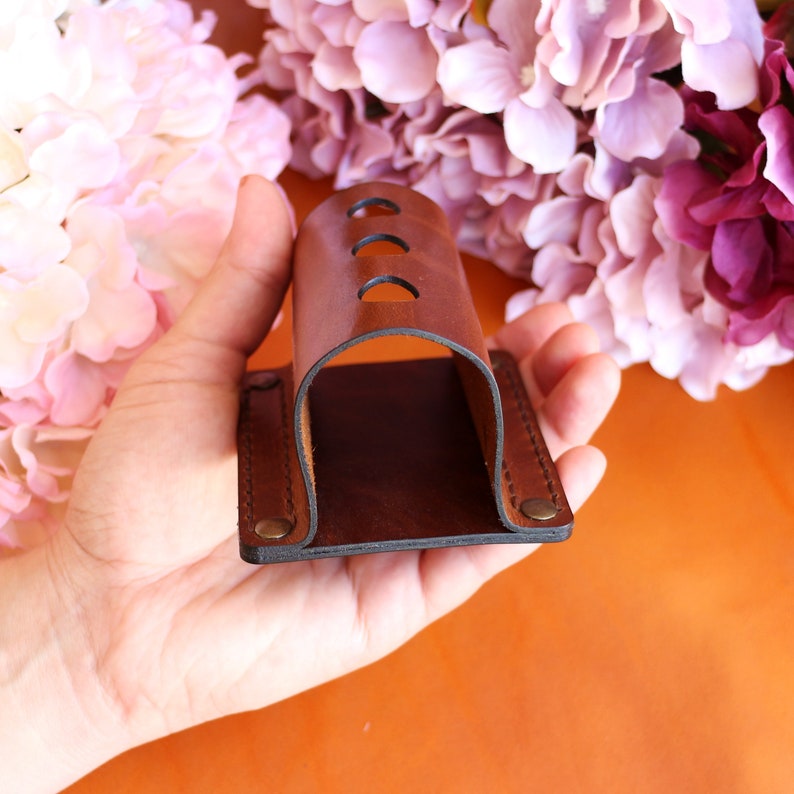 May include: A brown leather holder with three holes for storing items. The holder is held in a hand.