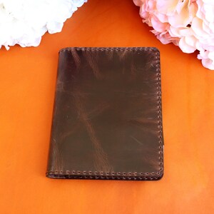 May include: A brown leather notebook with a stitched edge. The notebook is on a bright orange surface.