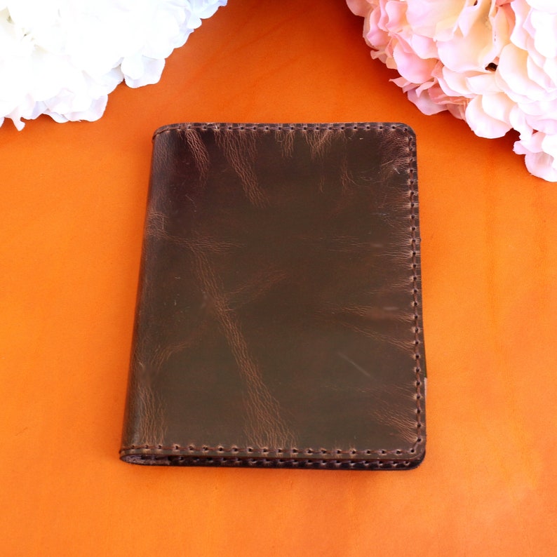May include: A brown leather notebook with a stitched edge. The notebook is on a bright orange surface.