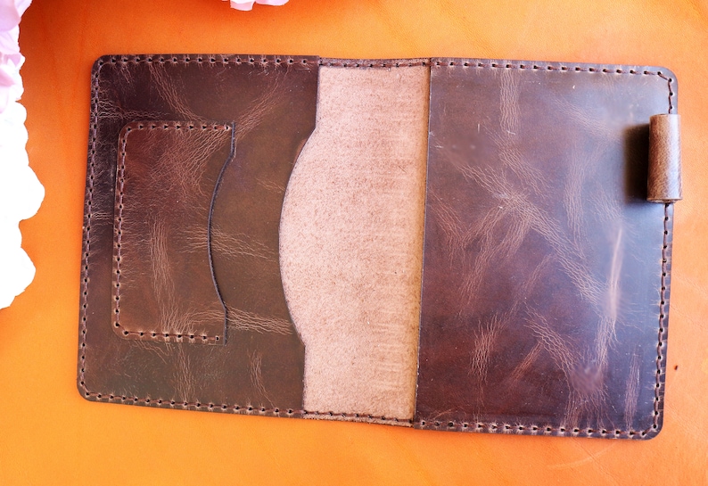 May include: A brown leather notebook cover with a stitched edge and a flap with a pocket. The cover has a worn, distressed look.
