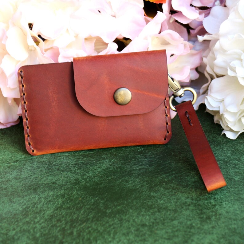 May include: A brown leather wallet with a flap closure and a metal button. The wallet has a key ring attached to it.