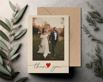May include: A wedding thank you card featuring a photograph of a bride and groom walking in a field. The card is beige with a red heart and the text "thank you" in cursive.