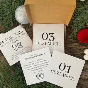 May include: A Christmas advent calendar for couples, presented in a brown box. The calendar features cards with dates and activities, with the numbers 01 and 03 visible. The background includes Christmas ornaments and greenery.