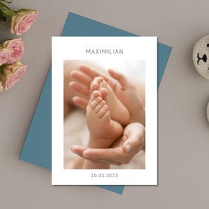 May include: A card with the name "MAXIMILIAN" and the date "30.05.2025" features a baby's feet held in hands. The card is on a blue envelope, with pink roses and white baby booties. A tender image.