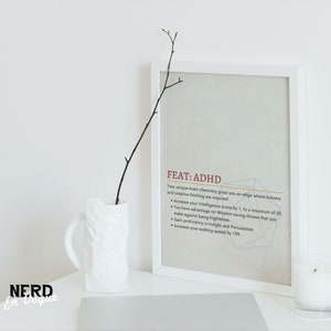 Puede incluir: Una impresi&oacute;n enmarcada en blanco con el texto "FEAT: ADHD" y una descripci&oacute;n de los beneficios de tener TDAH. La impresi&oacute;n est&aacute; sobre una superficie blanca con una taza blanca y una vela blanca.