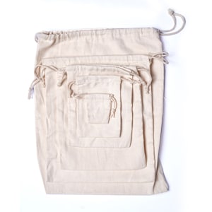 May include: Set of five natural cotton drawstring pouches in various sizes. The pouches are nested inside each other, with the largest pouch at the bottom and the smallest pouch at the top.