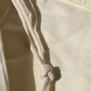 May include: Close-up of a natural-colored cotton drawstring bag with a knotted cord.