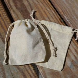 May include: Two white cotton drawstring pouches with a natural cotton cord. The pouches are lying on a wooden surface.