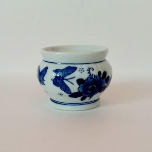 May include: A small white ceramic planter with a blue and white floral design. The planter features butterflies and flowers.