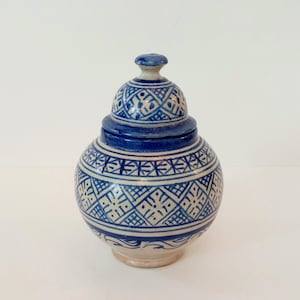 May include: A small, round ceramic jar with a lid. The jar is decorated with a blue and white geometric pattern. The lid is also decorated with a blue and white pattern.