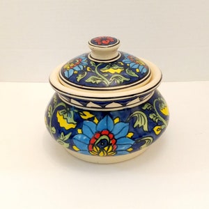 May include: A ceramic jar with a lid, decorated with a blue and white floral pattern. The lid has a red and yellow flower design.