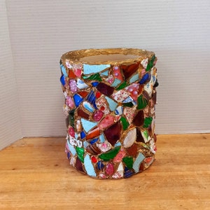 May include: A cylindrical vase made of gold-painted ceramic with a mosaic design. The mosaic is made of small pieces of broken ceramic in various colors, including blue, green, red, and white.