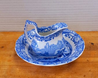 May include: A blue and white ceramic creamer and saucer set with a floral pattern. The creamer features a scene of a castle and a river.