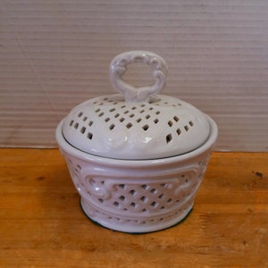 May include: White ceramic jar with a lid featuring a decorative, openwork design. The lid has a small, ornate handle.
