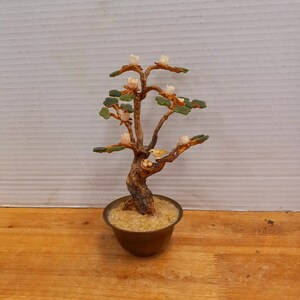 May include: A jade bonsai tree with white flowers and a small bird perched on a branch. The tree is potted in a brass pot with sand.
