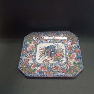 May include: A square ceramic serving platter with a blue and white floral design and a central image of a cart with a pink flower. The cart is drawn by a horse and has a blue and white design.
