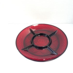 May include: A red glass serving dish with four sections and a central dip. The dish has a raised, textured design.