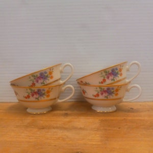 May include: Set of four vintage teacups with floral patterns and gold trim. The cups are stacked in pairs, with the top cup of each stack tilted slightly.