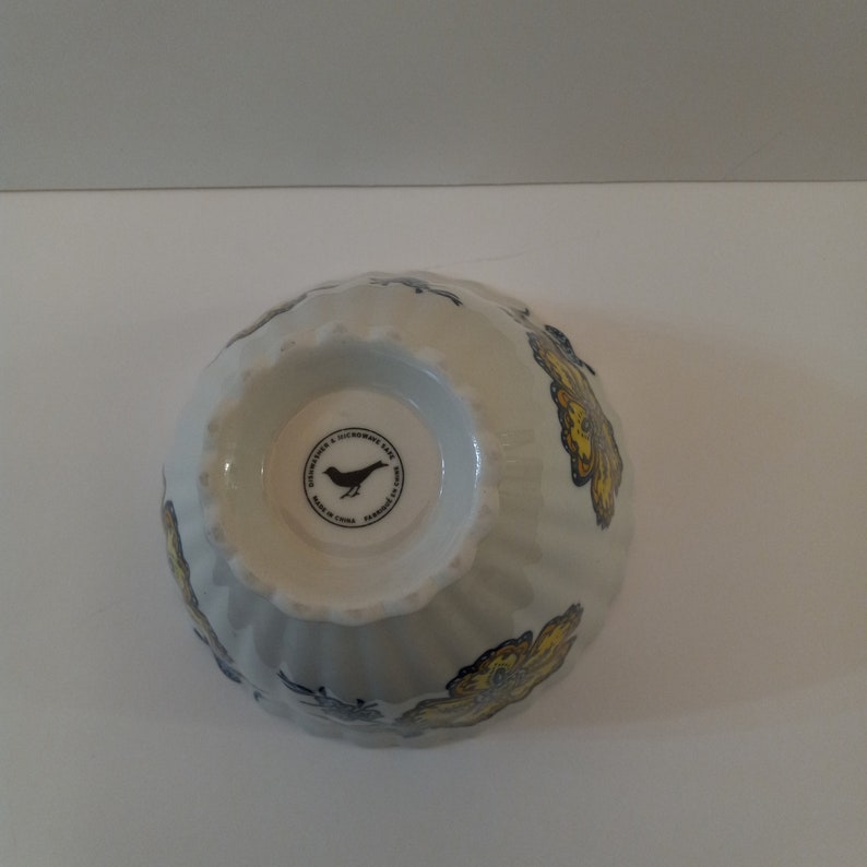 Może przedstawiać: Biała ceramiczna miska z wzorem ż&oacute;łtego i niebieskiego motyla. Na spodzie miski znajduje się czarne logo ptaka z tekstem "Department 56 & Microwave Safe, Made in China, Farmhouse, Farmington, MI".