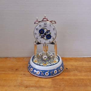 May include: A white porcelain Timex mantel clock with a blue and yellow floral design. The clock has a silver frame and a pendulum.